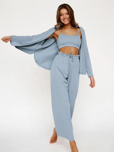 Femme souriante portant un ensemble nuisette élégant en bleu clair, composé d'un top sans manches et d'un pantalon large à taille élastiquée. Elle porte également une veste légère assortie, ajoutant une touche chic et décontractée. Elle pose joyeusement, mettant en valeur le confort et le style raffiné de cet ensemble.