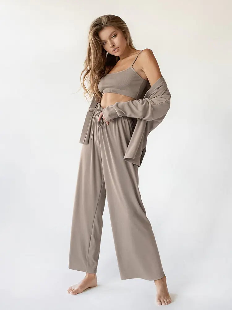 Femme portant un ensemble nuisette beige élégant et confortable, composé d'un top sans manches et d'un pantalon fluide à taille élastiquée. Elle porte également une veste légère assortie, créant un look à la fois décontracté et raffiné. Elle pose avec une attitude confiante, mettant en valeur le style simple et chic de cet ensemble.