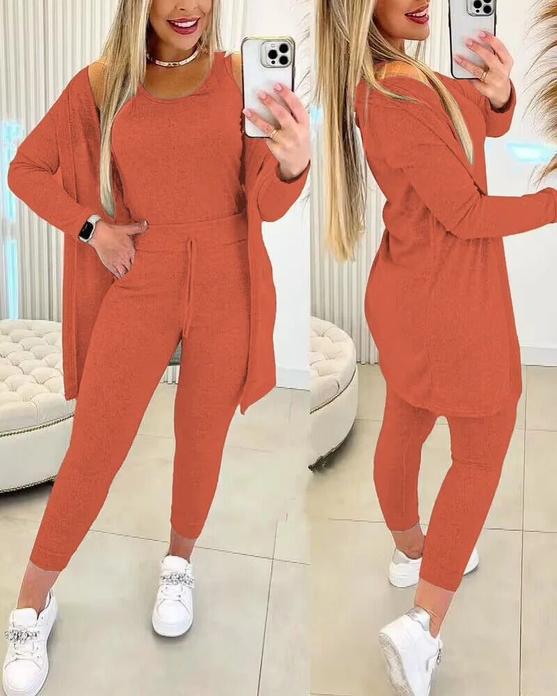 Femme portant l’ensemble Axelle en orange brique, composé d’un débardeur, d’un legging ajusté avec lien à la taille et d’un long cardigan fluide. Une tenue chic et cosy, parfaite pour la détente à la maison ou un style décontracté en ville.