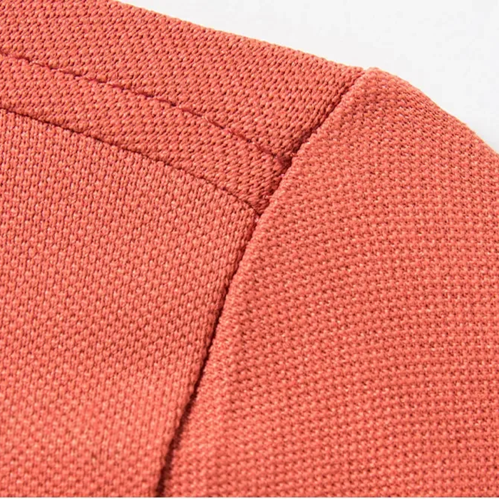 Gros plan sur le tissu d’un polo homme Abel couleur corail, avec une texture tricotée fine et des replis de la manche, illustrant la qualité du vêtement et son look élégant et confortable.