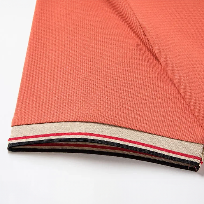Polo homme Abel couleur corail, à manches courtes avec col polo et poignets ornés d’un motif tartan beige/noir/rouge; coupe moderne et confortable, idéal pour un look estival.