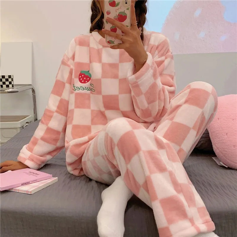 Femme portant un pyjama chaud à carreaux rose et blanc, décoré d’une fraise brodée accompagnée du mot sur le haut. Ensemble doux à manches longues avec pantalon assorti, idéal pour les soirées cocooning et les journées de détente à la maison.