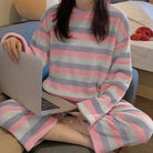 Femme portant un pyjama chaud à rayures horizontales roses, grises et blanches. Ensemble à manches longues avec pantalon assorti, en tissu doux et moelleux, parfait pour se détendre confortablement à la maison.