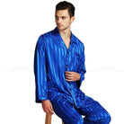Pyjama homme Adrien en satin bleu, à rayures élégantes, avec une chemise à manches longues et un pantalon assorti. Le modèle porte le pyjama avec une pose décontractée sur une chaise, offrant un look chic et confortable, idéal pour une nuit de repos.
