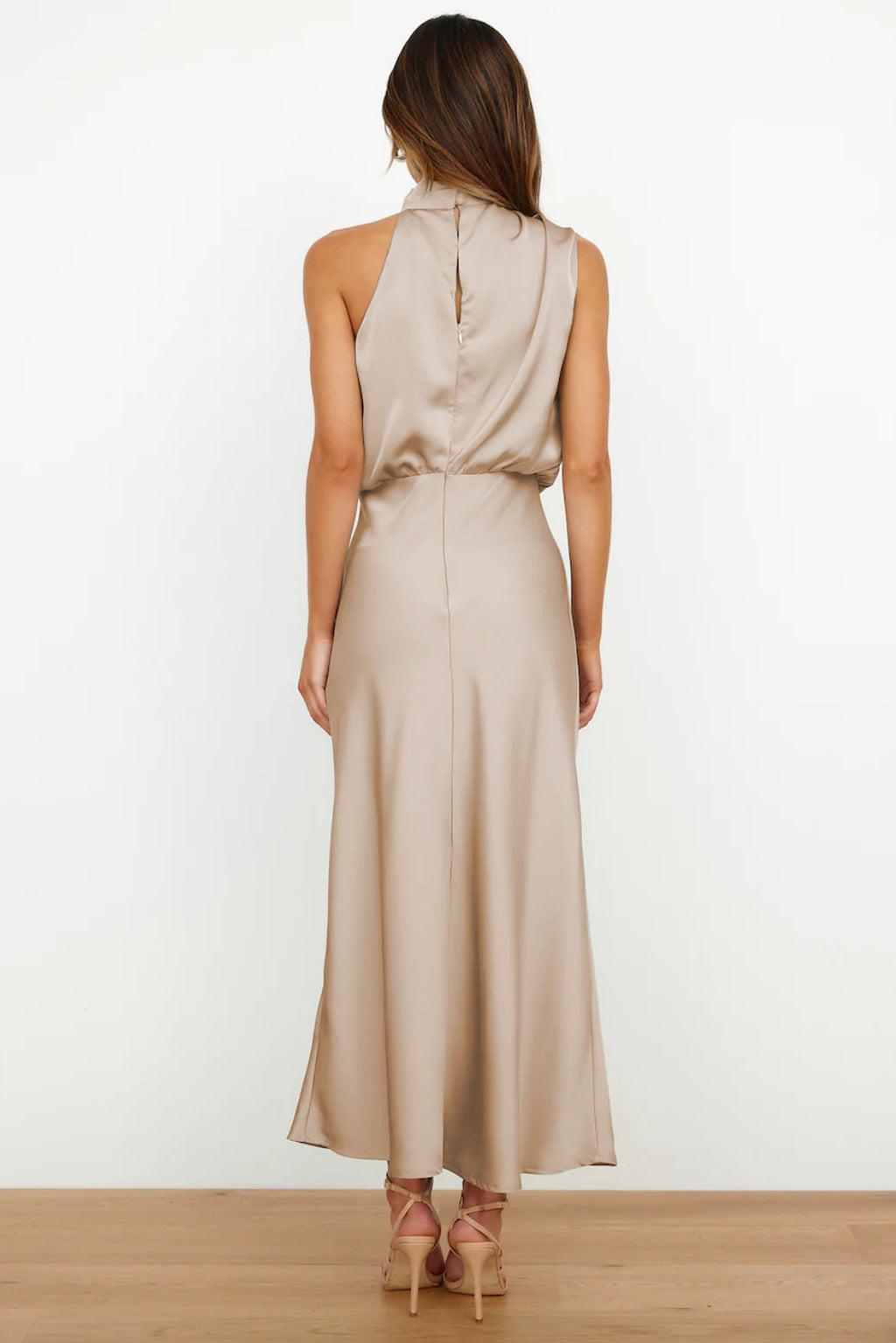 Vue de dos, cette robe longue beige en satin présente une coupe fluide, un détail de fermeture discrète à l&
