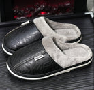 Chaussons homme Alan noirs, style pantoufles fermées avec effet cuir, col et intérieur doublés en fausse fourrure grise, semelle épaisse confortable pour garder les pieds au chaud à la maison.