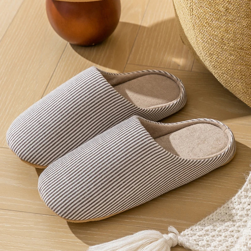 Chaussons d’intérieur unisexes Alban antidérapants, coloris beige à fines rayures, posés sur parquet dans un salon, avec intérieur rembourré et semelle confortable.