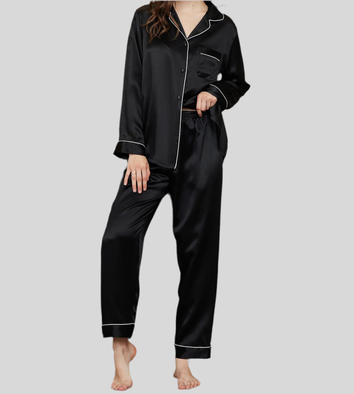 Femme portant un pyjama deux pièces noir en satin brillant, composé d’un haut boutonné à col classique et passepoils blancs, et d’un pantalon long assorti à taille élastique. Ensemble soyeux, élégant et confortable, idéal pour passer des nuits douces avec style.