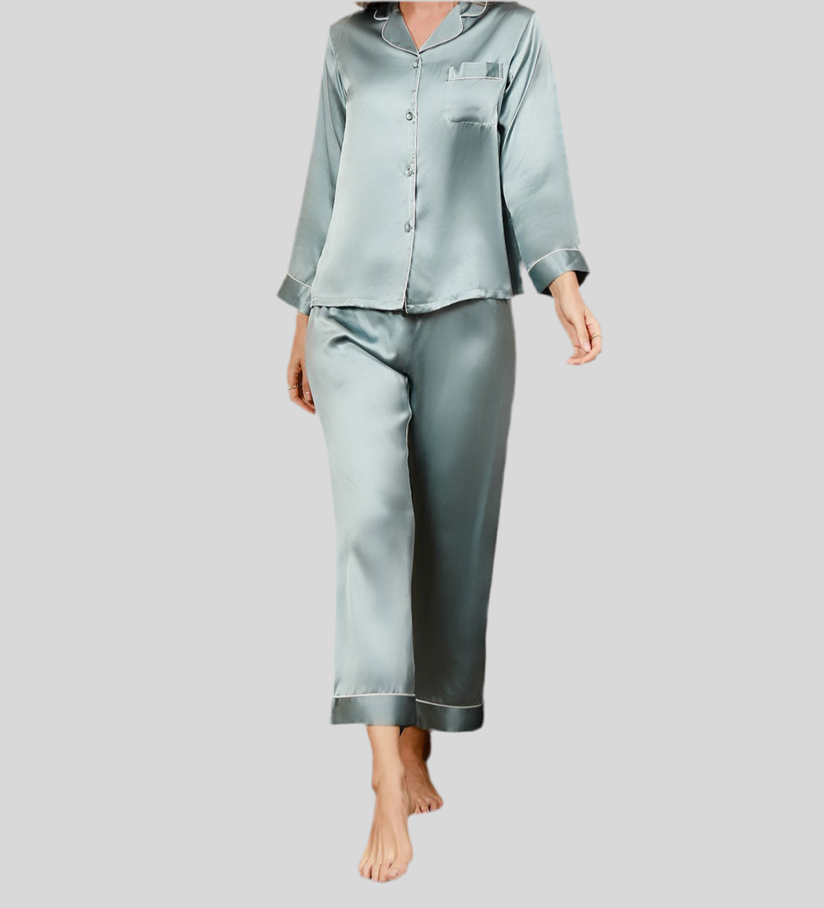 Femme portant un pyjama deux pièces en satin vert sauge, composé d’un haut à manches longues avec col classique, fermeture boutonnée et passepoils fins, accompagné d’un pantalon fluide assorti. Ensemble élégant et soyeux, parfait pour des nuits paisibles avec style.