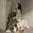 Femme assise dans une ambiance cosy, vêtue du pyjama Amélie, un ensemble élégant et tendance en tissu duveteux vert kaki avec motif géométrique, parfait pour des moments de détente stylés à la maison.