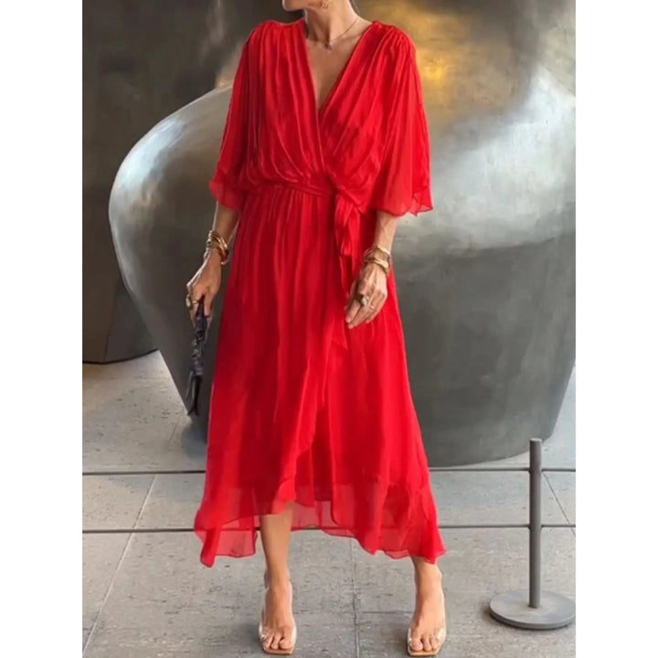 Rouge fluide, décolleté cache-cœur, manches amples et ceinture nouée à la taille, longueur midi avec ourlet volanté, tenant une pochette.
