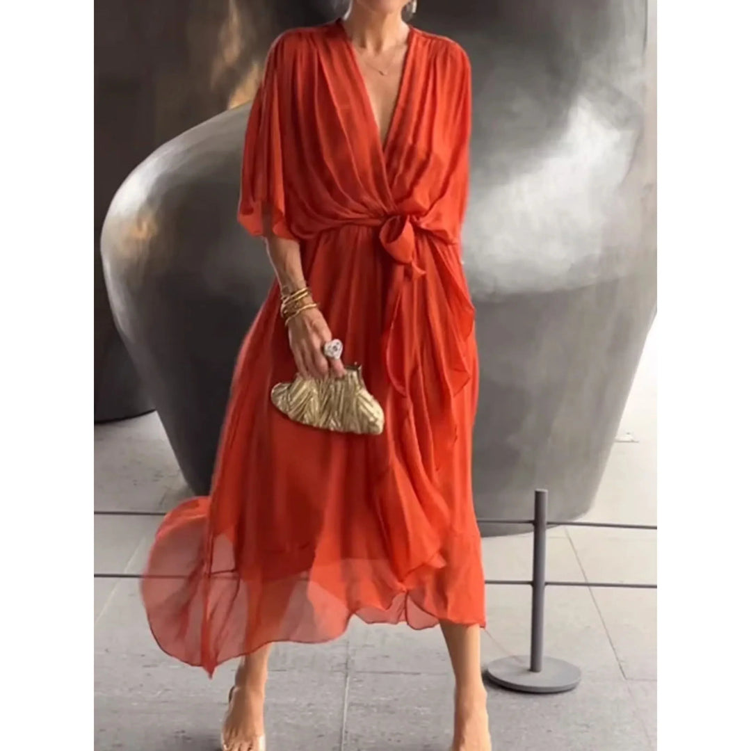 Orange brûlé fluide, décolleté cache-cœur, manches amples et ceinture nouée à la taille, longueur midi avec ourlet volanté, avec pochette dorée.