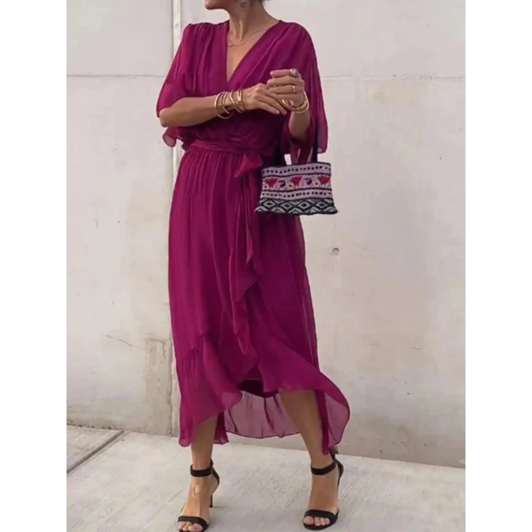 Fuchsia, décolleté cache-cœur, manches amples et ceinture nouée à la taille, ourlet asymétrique volanté, avec sandales à talons et sac brodé.
