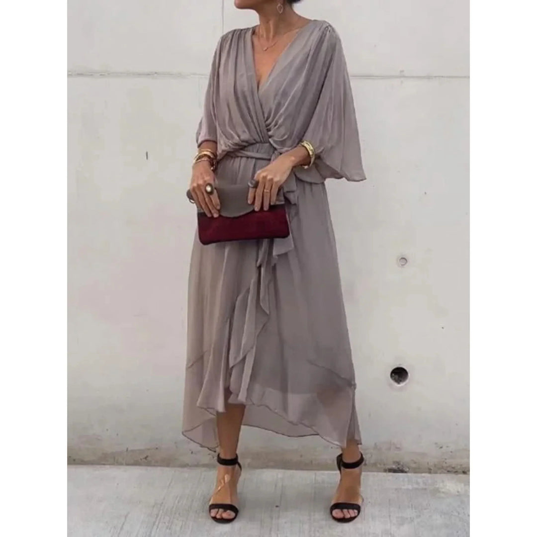 Gris taupe fluide, décolleté cache-cœur, manches amples et ceinture nouée à la taille, ourlet asymétrique volanté, avec sandales à talons et pochette.