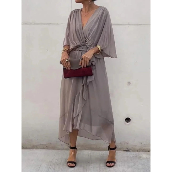 Gris taupe fluide, décolleté cache-cœur, manches amples et ceinture nouée à la taille, ourlet asymétrique volanté, avec sandales à talons et pochette.