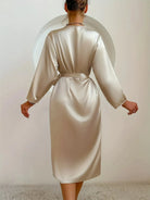 Vue de dos d’une femme portant un peignoir satiné couleur champagne, à manches longues et ceinture nouée à la taille. Modèle fluide, sobre et élégant, idéal pour une tenue de détente chic et confortable à la maison.