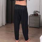 Vue arrière d’un homme portant le pantalon de pyjama en satin pour homme Amaury, pantalon noir à fines rayures avec taille élastique, coupe fluide et tissu doux offrant un confort optimal et une sensation soyeuse idéale pour la nuit ou les moments de détente à la maison.