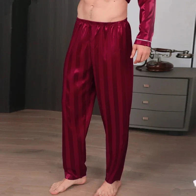 Vue de trois-quarts d’un homme portant le pantalon de pyjama en satin pour homme Amaury, pantalon bordeaux satiné à fines rayures avec taille élastique souple, coupe fluide et confortable, offrant une sensation douce, légère et élégante pour le sommeil ou les moments de détente à la maison.