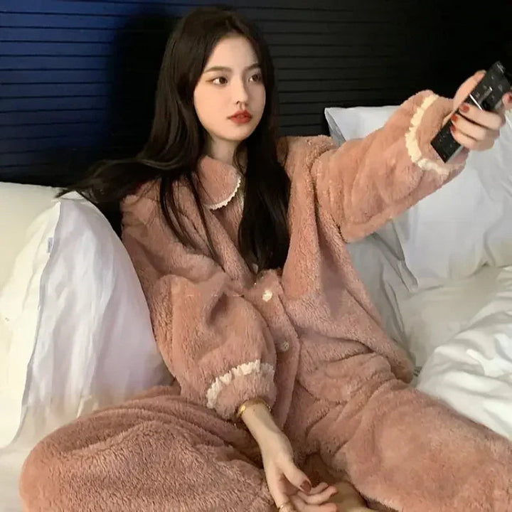 Femme assise sur un lit, vêtue d’un pyjama polaire rose avec détails en dentelle crème au col et aux poignets. Pyjama boutonné au style cosy et élégant, conçu pour offrir chaleur et confort lors des soirées hivernales à la maison.