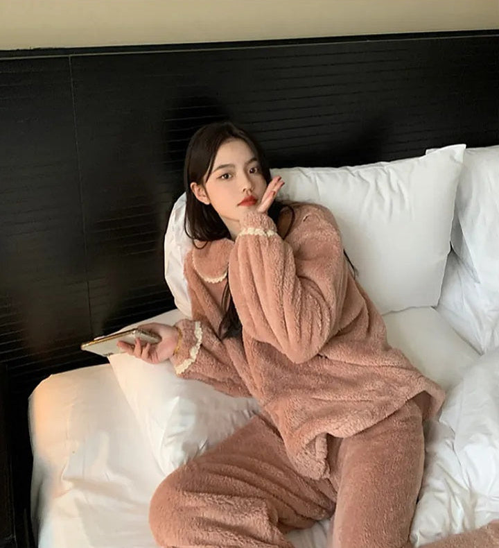 Jeune femme allongée sur un lit, vêtue d’un pyjama polaire rose avec col rond à bordure en dentelle crème. Ensemble deux pièces doux et épais, parfait pour rester au chaud avec style pendant les journées froides à la maison.