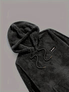 Haut de pyjama teddy noir pour homme avec capuche et cordon, fabriqué dans un tissu polaire doux et épais. Détail brodé sur la poitrine. Vêtement confortable et chaud, parfait pour l’hiver et les moments de détente à la maison.