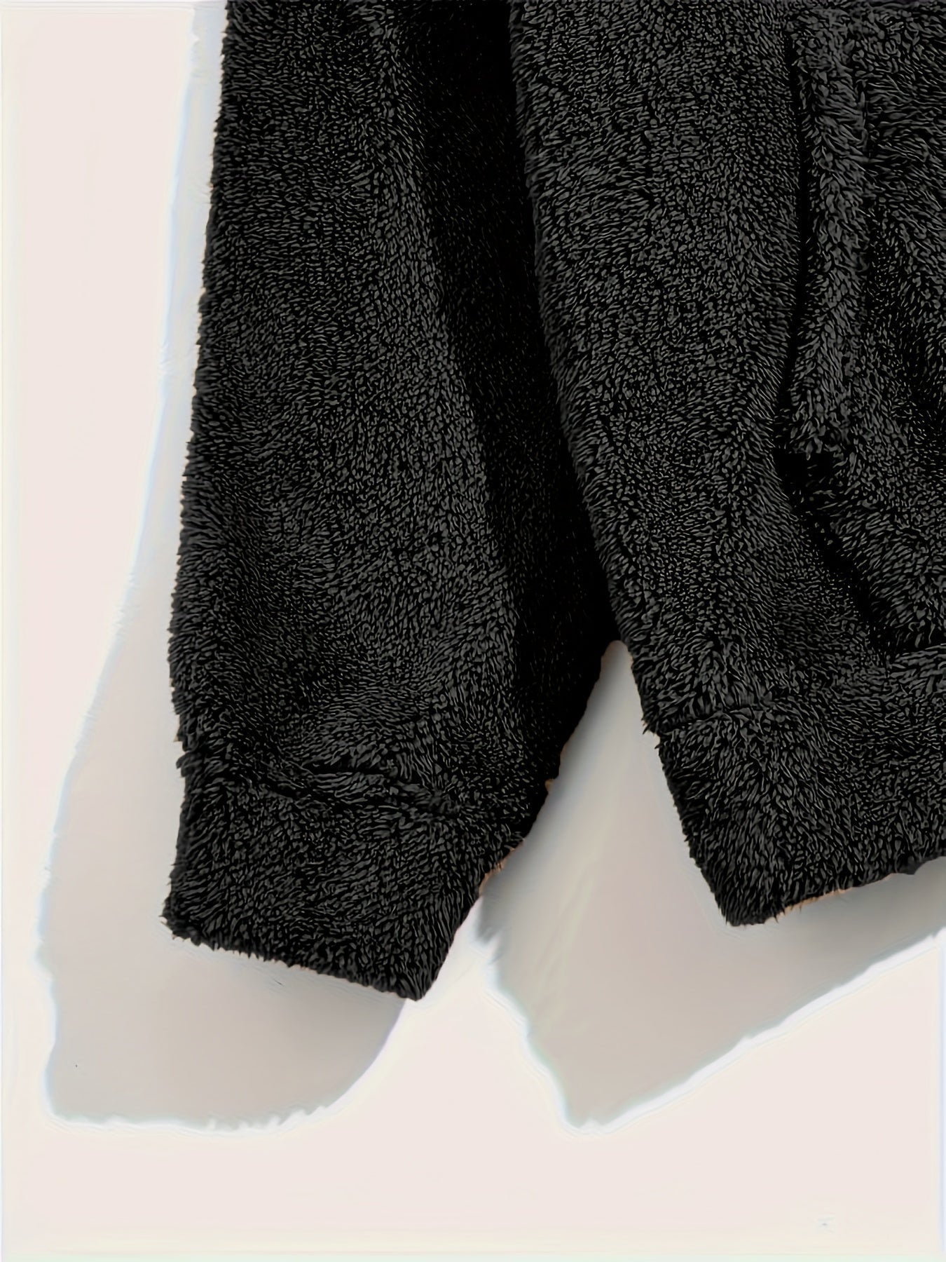 Gros plan sur la manche et la poche d’un pyjama teddy noir pour homme. Tissu épais et ultra doux, idéal pour rester au chaud et confortable pendant les nuits froides ou les journées détente à la maison.