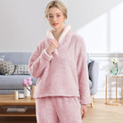 Femme portant un pyjama polaire rose poudré composé d’un haut doux à col large doublé en sherpa blanc et d’un pantalon assorti. Ensemble chaud, moelleux et très confortable, idéal pour l’hiver et les moments cocooning à la maison.