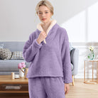 Femme portant un pyjama polaire violet lavande composé d’un haut doux à col large doublé en sherpa beige et d’un pantalon assorti. Ensemble chaud, moelleux et très confortable, idéal pour l’hiver et les moments cocooning à la maison.