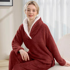 Femme assise portant un pyjama polaire rouge bordeaux composé d’un haut doux à col large doublé en sherpa blanc et d’un pantalon assorti. Ensemble chaud, moelleux et très confortable, idéal pour l’hiver et les moments cocooning à la maison.