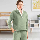 Femme portant un pyjama polaire vert sauge composé d’un haut doux à col large doublé en sherpa blanc et d’un pantalon assorti. Ensemble chaud, moelleux et très confortable, idéal pour les soirées cocooning et l’hiver.