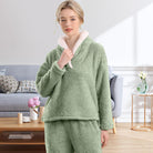 Femme portant un pyjama polaire vert sauge avec un haut doux à col large doublé en sherpa blanc et un pantalon assorti. Ensemble chaud, moelleux et très confortable, parfait pour l’hiver et les moments cocooning à la maison.