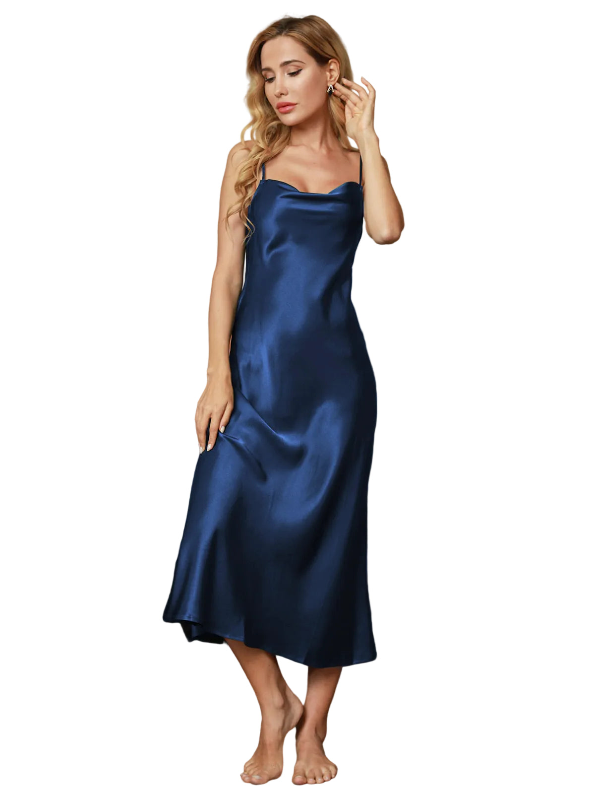 modèle portant une nuisette satinée bleu marine à fines bretelles, coupe midi fluide avec encolure drapée, debout près d’un fauteuil orange.