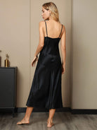 vue de dos d’une nuisette satinée noire à fines bretelles, coupe midi fluide, portée dans un intérieur moderne.