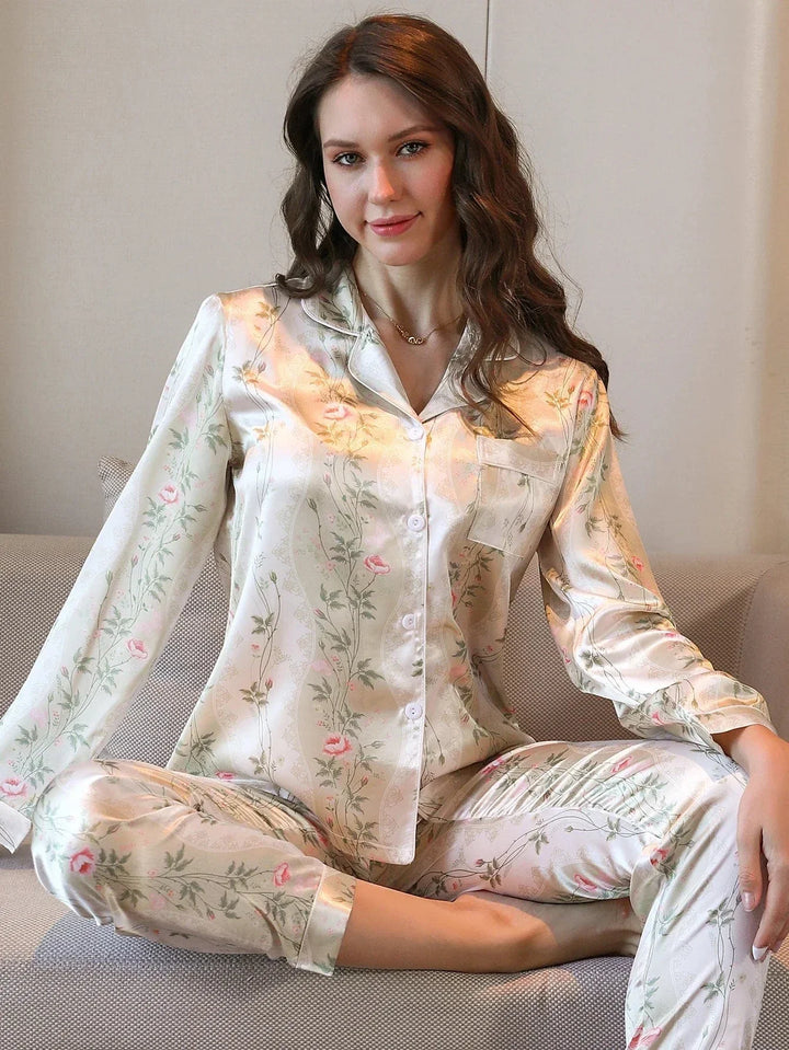 Pyjama en satin pour femme, décoré de motifs floraux délicats dans des tons de rose sur fond crème. Sur cette photo, une femme porte ce pyjama élégant et confortable, assise sur un canapé avec un sourire détendu. Ce pyjama est parfait pour des moments de détente à la maison, alliant confort, douceur et raffinement.