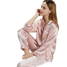 Femme assise en position détendue, portant un pyjama en satin rose clair à manches longues et col à revers. Ensemble élégant et doux au toucher, parfait pour les nuits paisibles et les moments de détente à la maison.