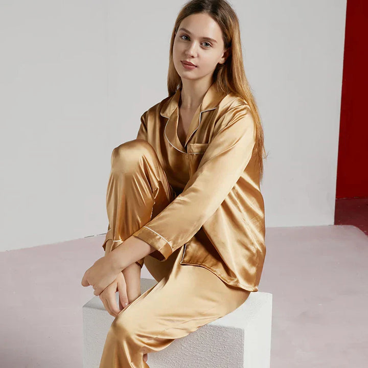 Femme assise portant un pyjama en satin doré brillant, à manches longues et col à revers avec passepoils. Ensemble luxueux, fluide et confortable, parfait pour des nuits douces ou des instants de détente raffinés à la maison.