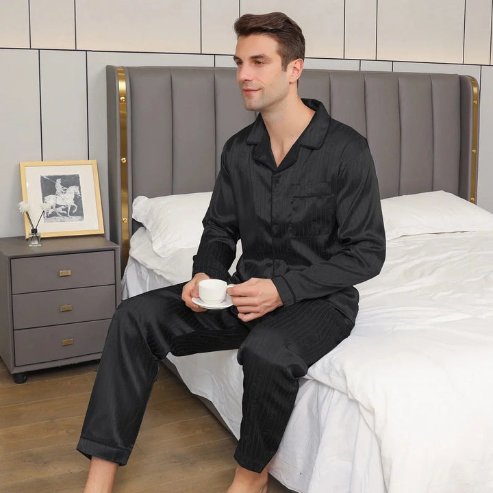 Homme portant le pyjama satin homme Aymeric noir, chemise à manches longues et pantalon assorti, présenté dans une chambre, style élégant et confortable.
