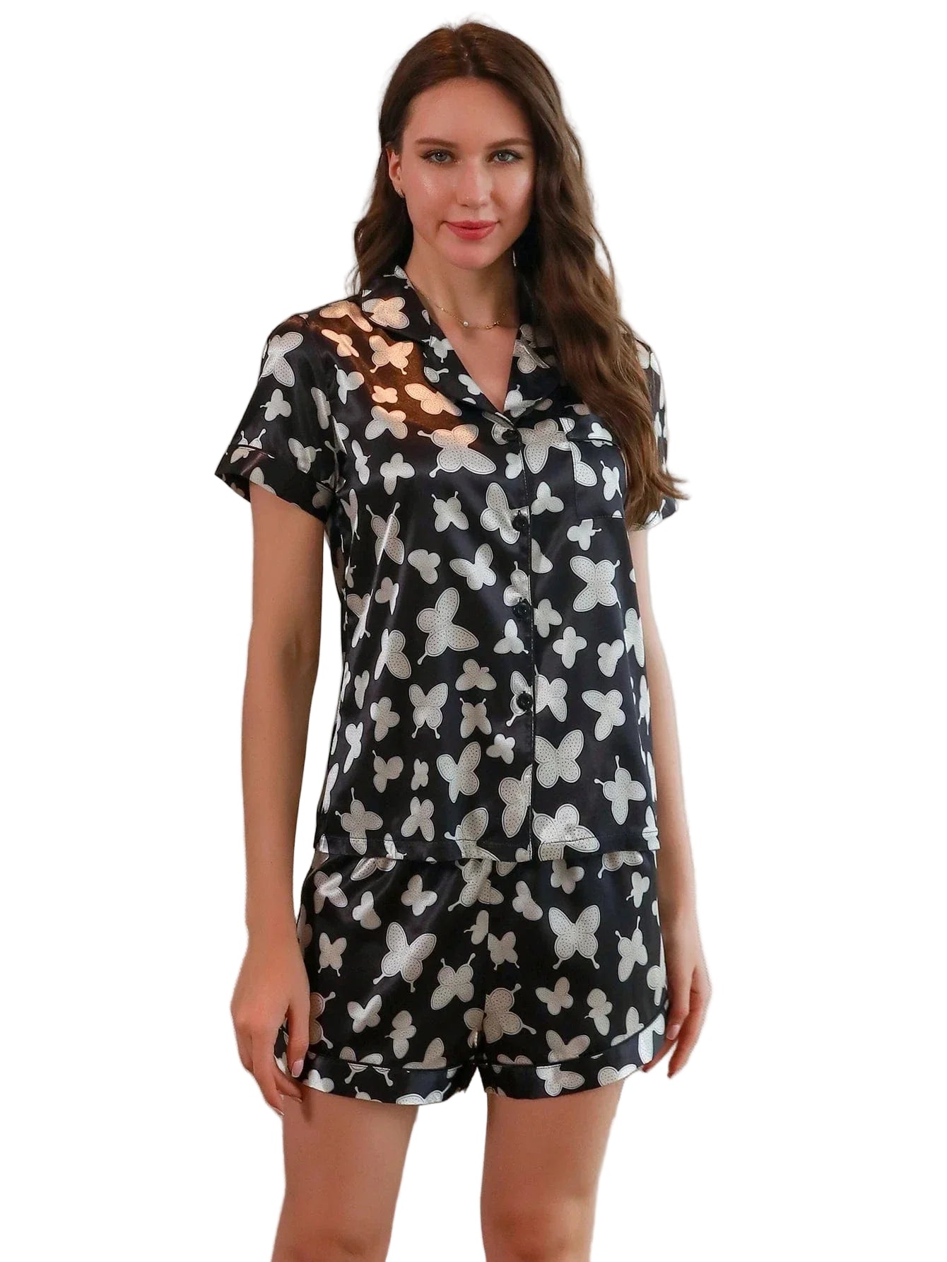 Femme portant le pyjama court femme, un ensemble satiné léger et agréable composé d’une chemise à manches courtes et d’un short noir à motifs blancs, présenté dans un intérieur moderne et lumineux.