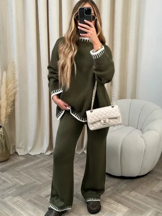Femme prenant un selfie en portant un ensemble lounge vert kaki avec finitions blanches contrastantes au col, poignets et ourlets. L’ensemble comprend un pull ample à manches longues et un pantalon droit assorti. Style confortable, chic et décontracté, complété par un sac à main matelassé beige pour un look moderne et tendance.