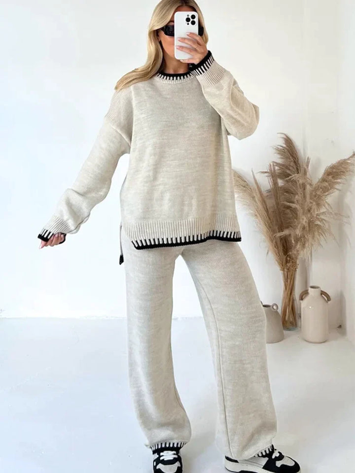Femme prenant un selfie en portant un ensemble lounge beige clair avec finitions côtelées noires au col, poignets et ourlets. Le set comprend un pull ample à manches longues et un pantalon fluide assorti. Tenue douce, élégante et décontractée, idéale pour un style cosy au quotidien.