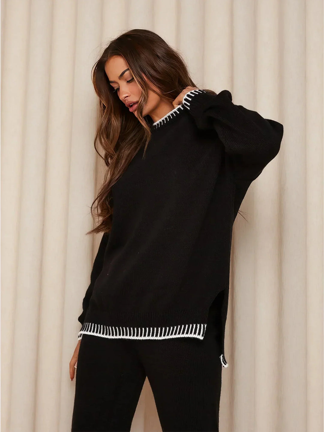 Femme portant un ensemble lounge noir composé d’un pull à manches longues et d’un pantalon assorti, avec finitions contrastantes blanches au col et à l’ourlet. Tenue élégante, douce et confortable, parfaite pour un style chic et décontracté à la maison comme à l’extérieur.