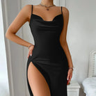 Femme portant la nuisette longue Belinda noire, avec fines bretelles, encolure drapée et fente haute sur le côté. Lingerie satinée, chic et confortable, idéale pour une allure sensuelle et raffinée à la maison ou pour des occasions spéciales.