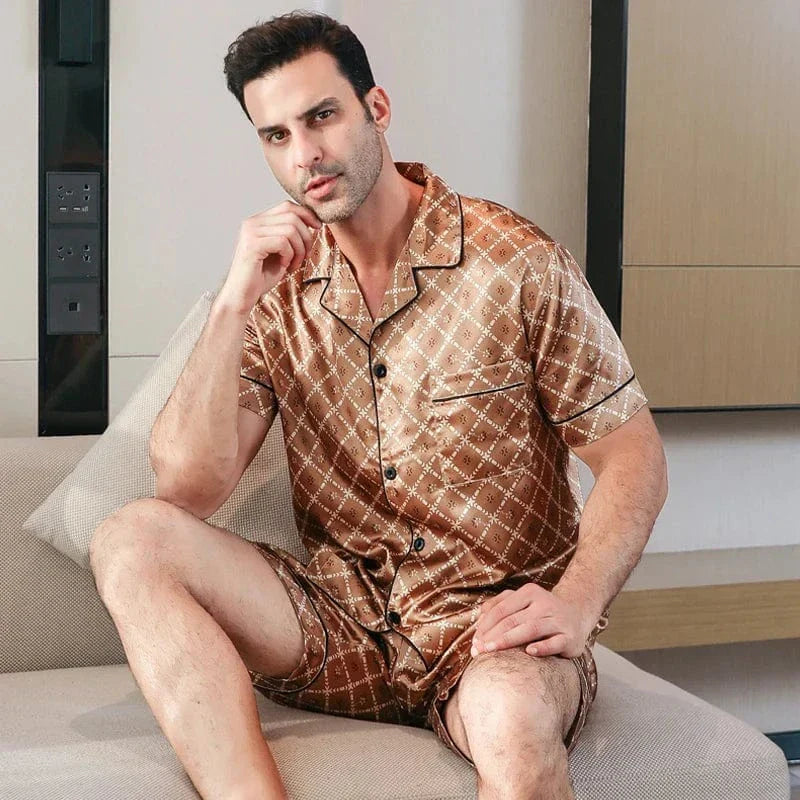 Homme assis portant le pyjama court satin Bernard pour homme, ensemble deux pièces avec chemise boutonnée à manches courtes et short assorti, motif géométrique marron, présenté en intérieur.