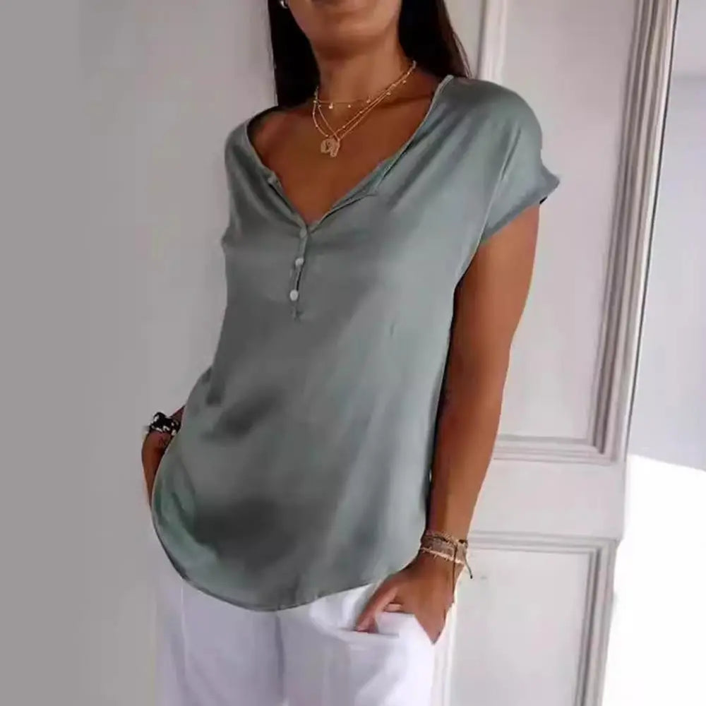 Haut Bliss pour femme, élégant et confortable, coupe fluide à manches courtes, coloris vert avec encolure en V et boutons, porté avec un pantalon blanc pour un style chic et décontracté.