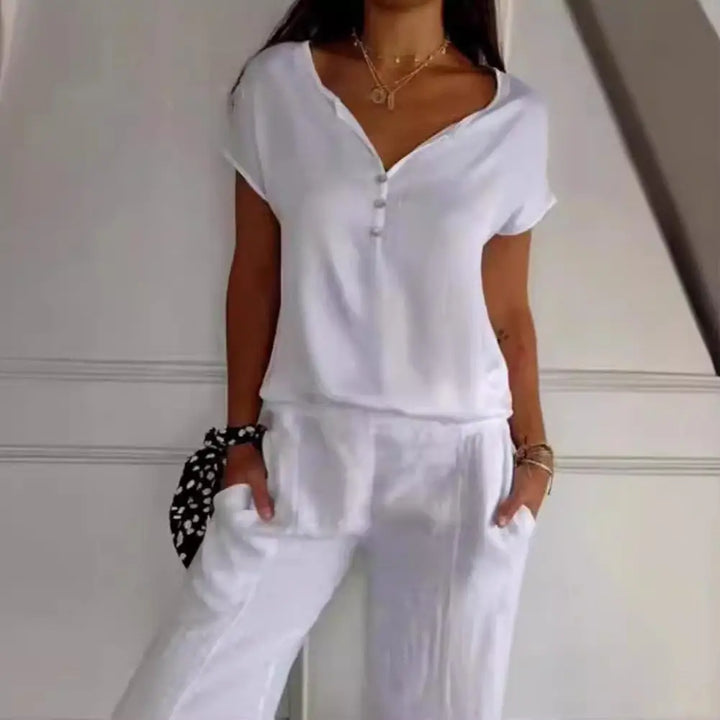 Haut Bliss pour femme, élégant et confortable, coupe fluide à manches courtes, coloris blanc avec encolure en V et boutons, porté avec un pantalon assorti pour un look chic et décontracté.