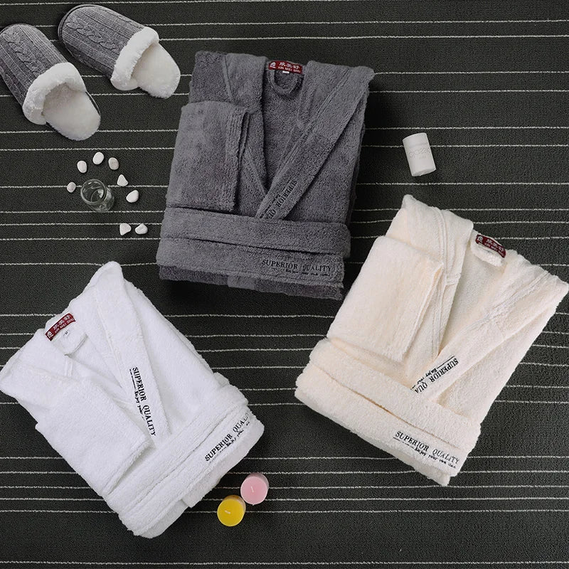 Trois peignoirs Cédric pour homme, modèles doux et relaxants, présentés pliés sur un tapis sombre : un gris, un beige et un blanc, accompagnés de chaussons et d’accessoires bien-être.