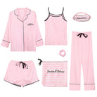 Ensemble de pyjama femme Célia, doux et élégant, composé de plusieurs pièces roses à rayures blanches : chemise à manches longues, débardeur, pantalon, short, masque de nuit, chouchou et pochette assortie, disposés à plat sur fond blanc.