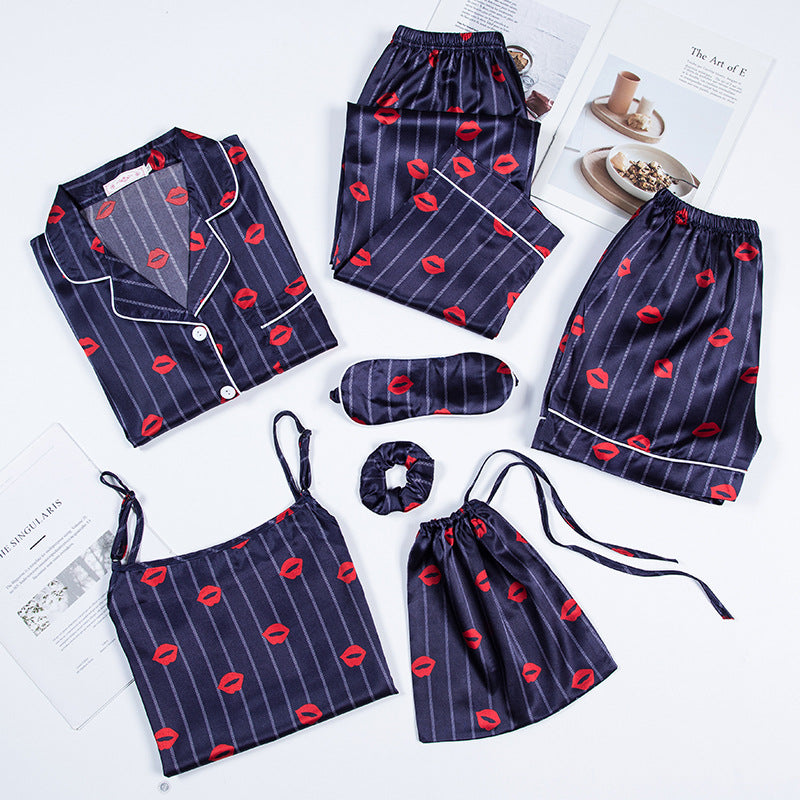 Ensemble de pyjama femme Célia, doux et élégant, composé de plusieurs pièces en satin bleu nuit à rayures et imprimé lèvres rouges : chemise à boutons, débardeur, pantalon, short, masque de nuit, chouchou et pochette assortie, soigneusement disposés à plat sur un fond blanc.