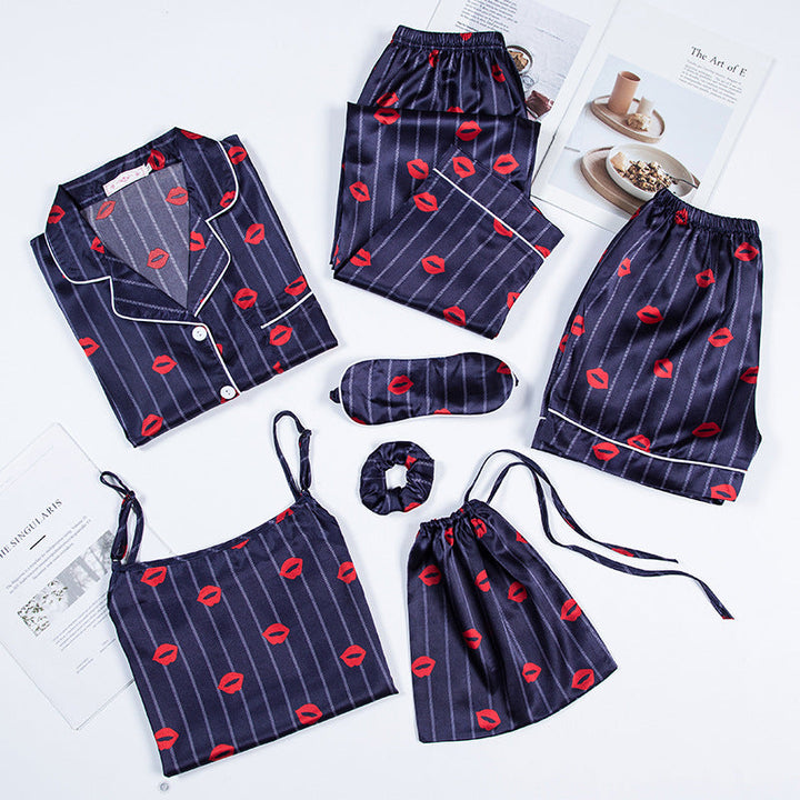Ensemble de pyjama femme Célia, doux et élégant, composé de plusieurs pièces en satin bleu nuit à rayures et imprimé lèvres rouges : chemise à boutons, débardeur, pantalon, short, masque de nuit, chouchou et pochette assortie, soigneusement disposés à plat sur un fond blanc.