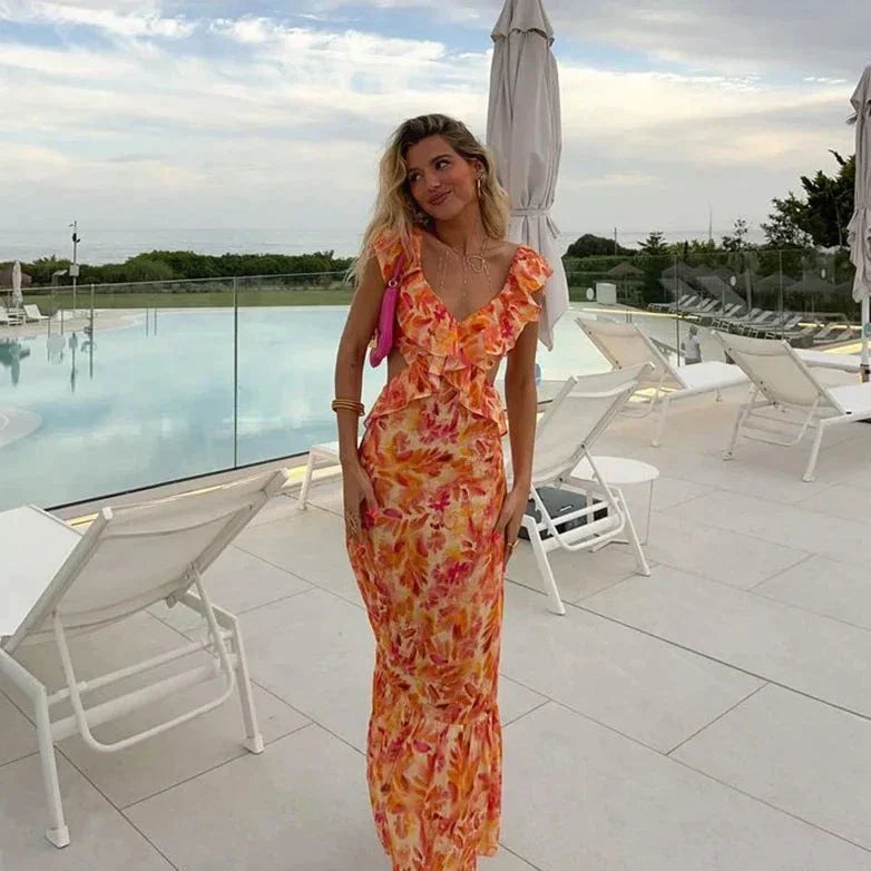 Robe maxi femme Calais fluide à imprimé floral orangé et rose avec détails volantés au décolleté, portée au bord d’une piscine pour un style élégant, féminin et estival.